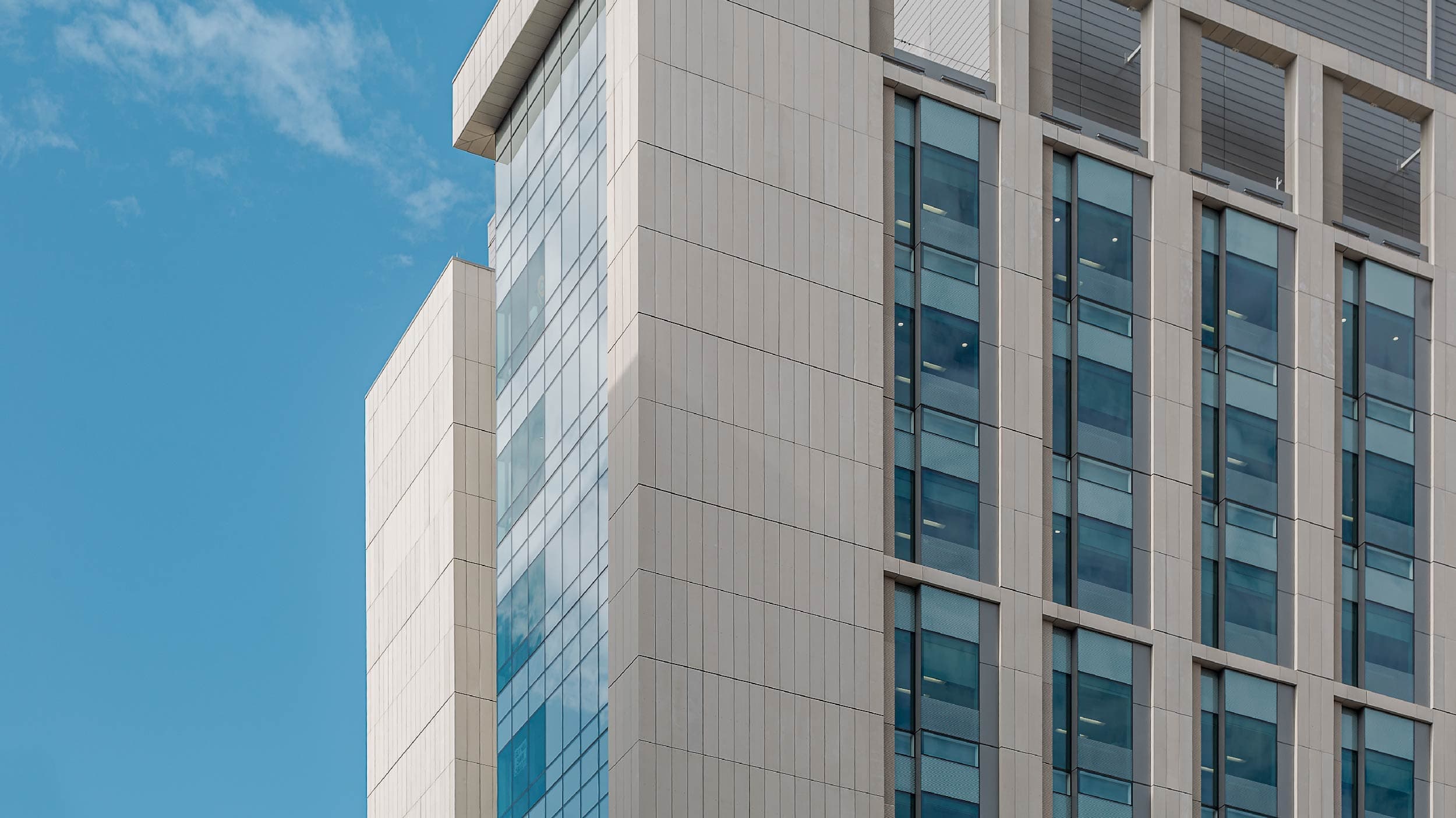 Pale TAKTL architectural UHPC panels, glass and deep facade reveals at a building corner